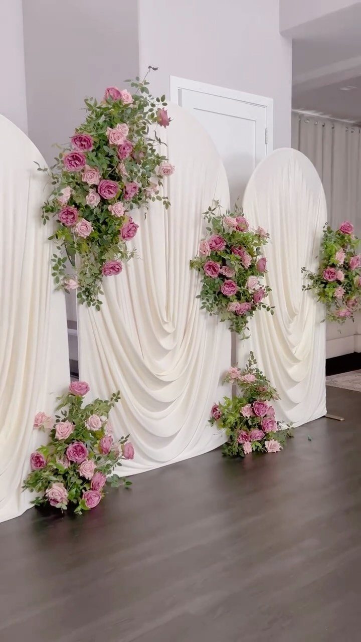 White fabric drapery arranged in elegant arches decorated with pink roses and green foliage.