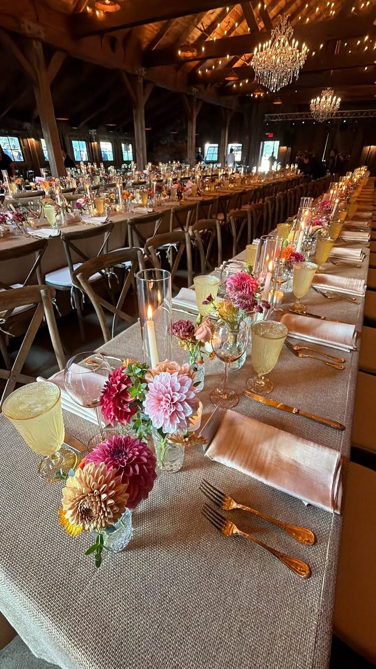 Long wedding reception table decorated with colorful floral arrangements in small glass vases and lit candles.