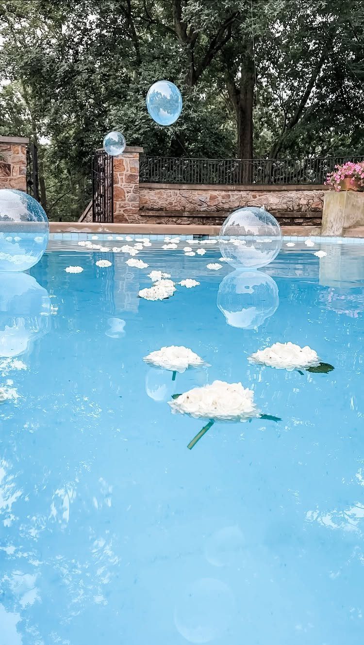 White flowers and clear spheres floating on the surface of a bright blue swimming pool.