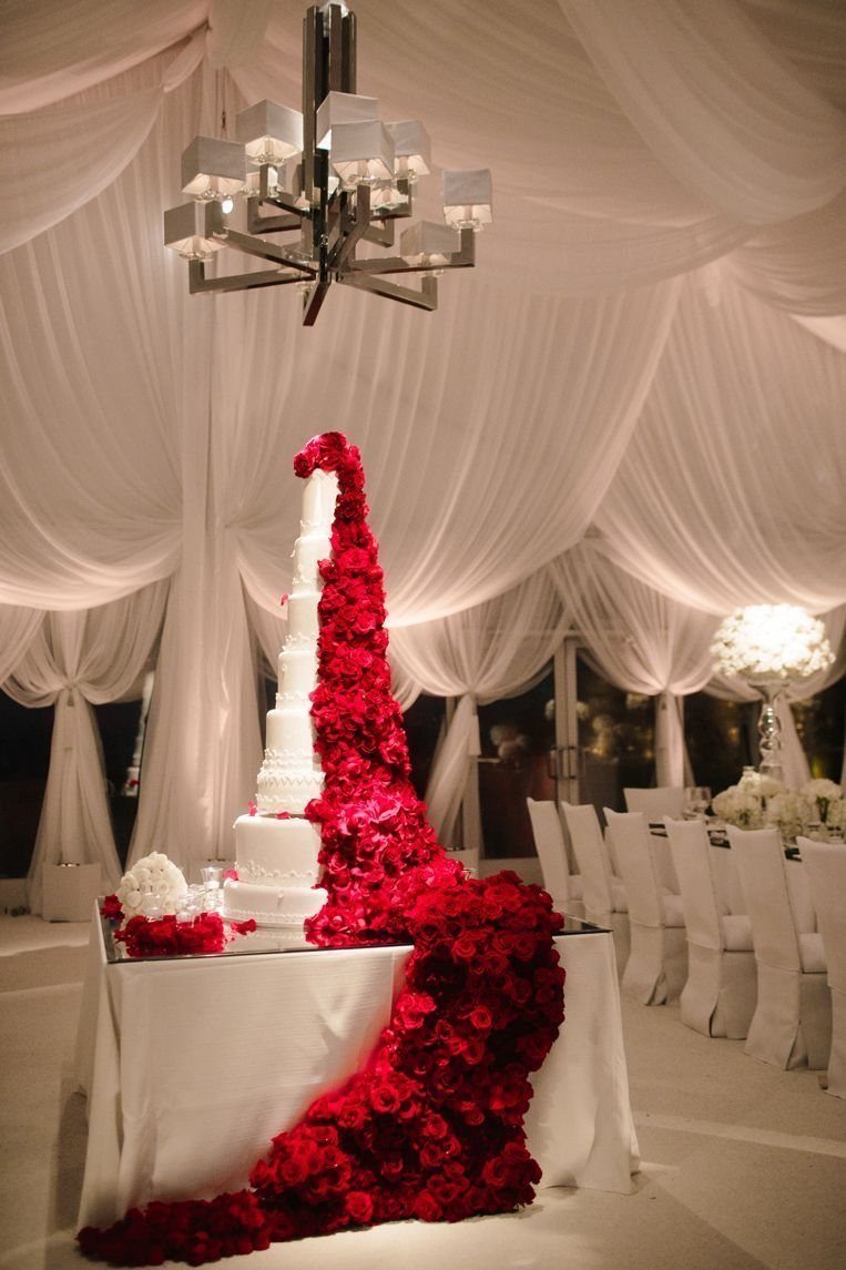 Wedding Decor with Red Roses: 9 Concepts from Pew Markers to Car Details 4 A white wedding cake decorated with a cascading trail of red roses flowing onto the table.