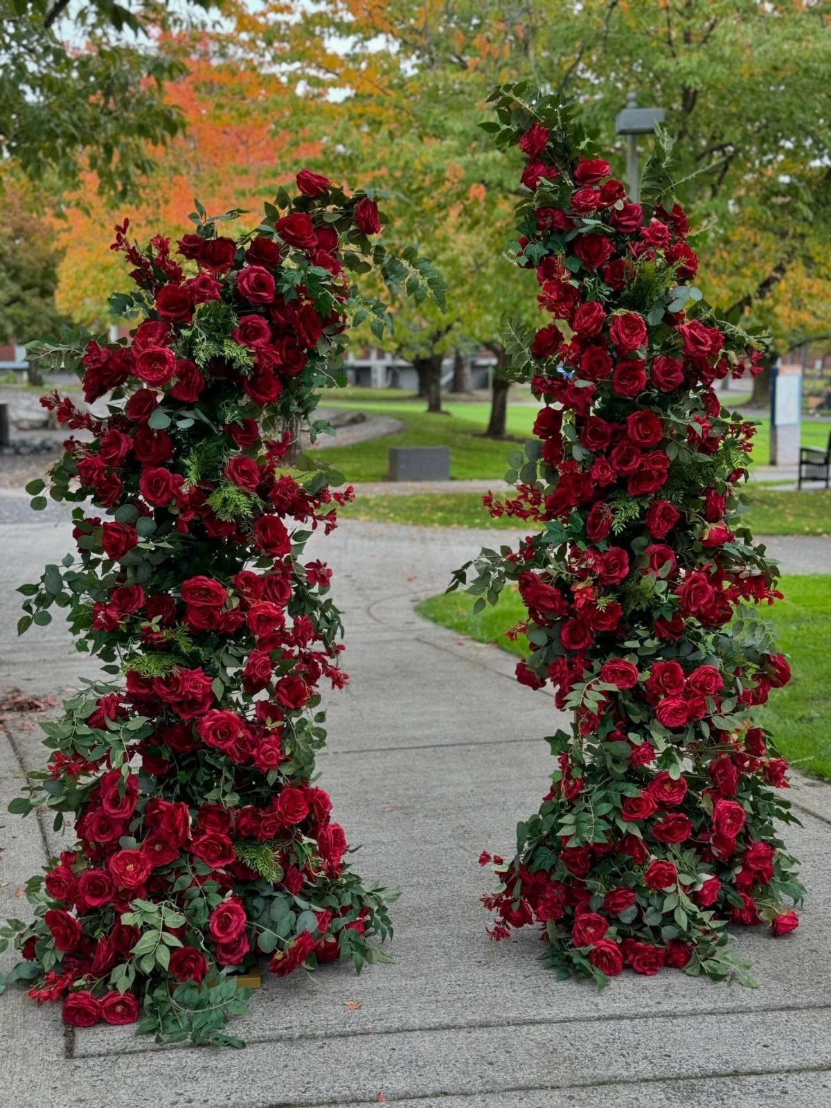 Wedding Decor with Red Roses: 9 Concepts from Pew Markers to Car Details 8 Two tall pillars of red roses and green leaves standing on a paved path outdoors.