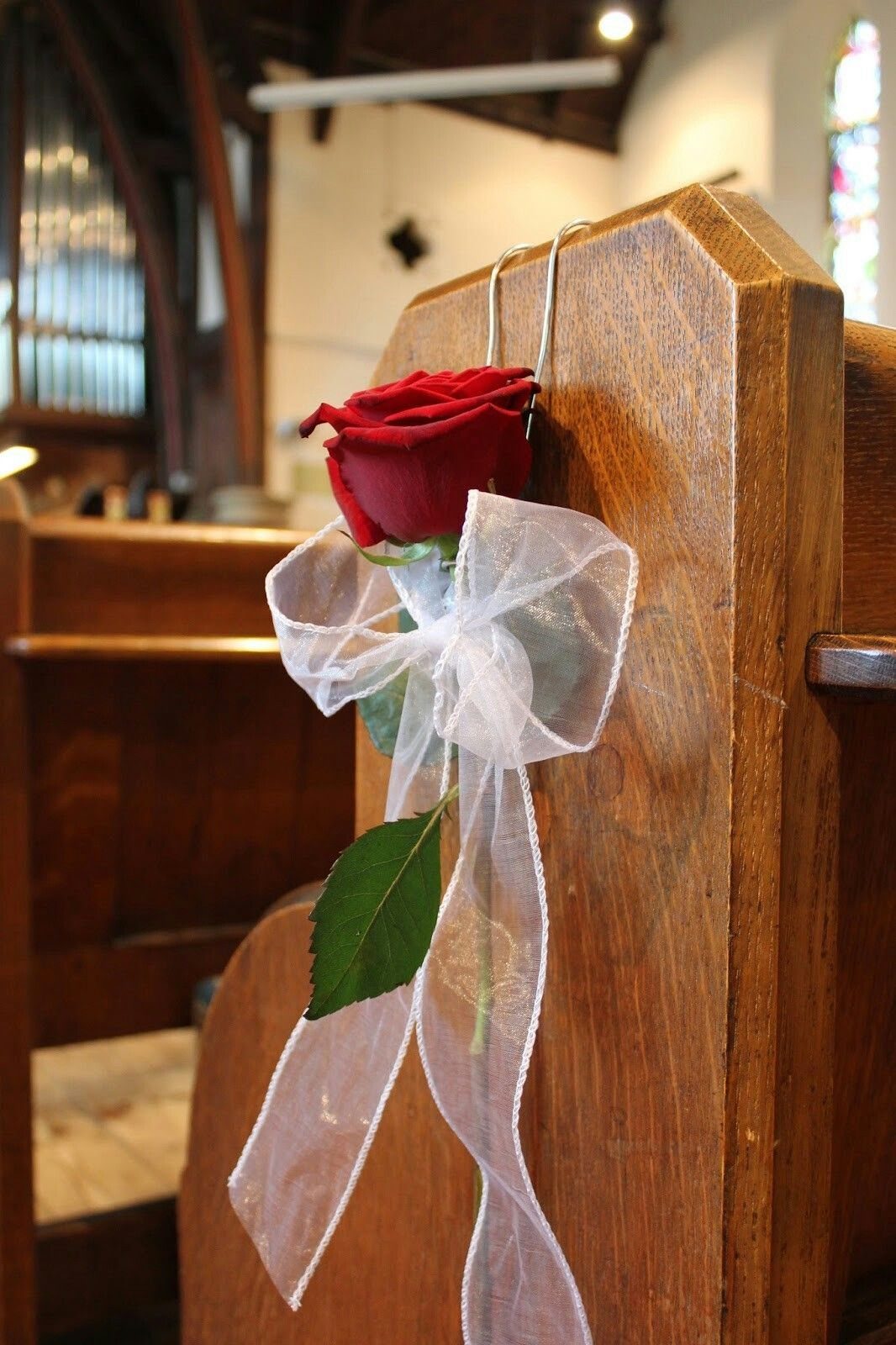 Wedding Decor with Red Roses: 9 Concepts from Pew Markers to Car Details 5 A single red rose with a white tulle bow attached to a wooden church pew.