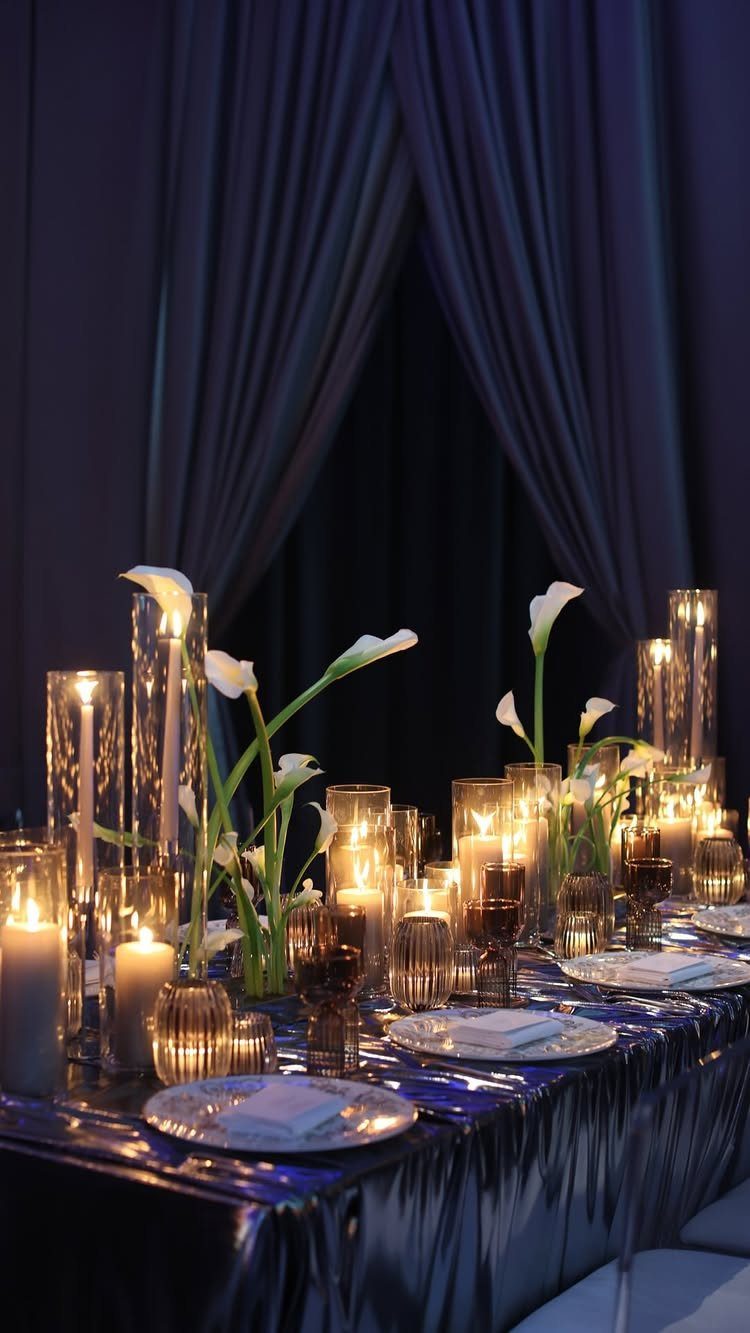 A formal dining table featuring dark blue shimmering linens and white calla lily centerpieces.