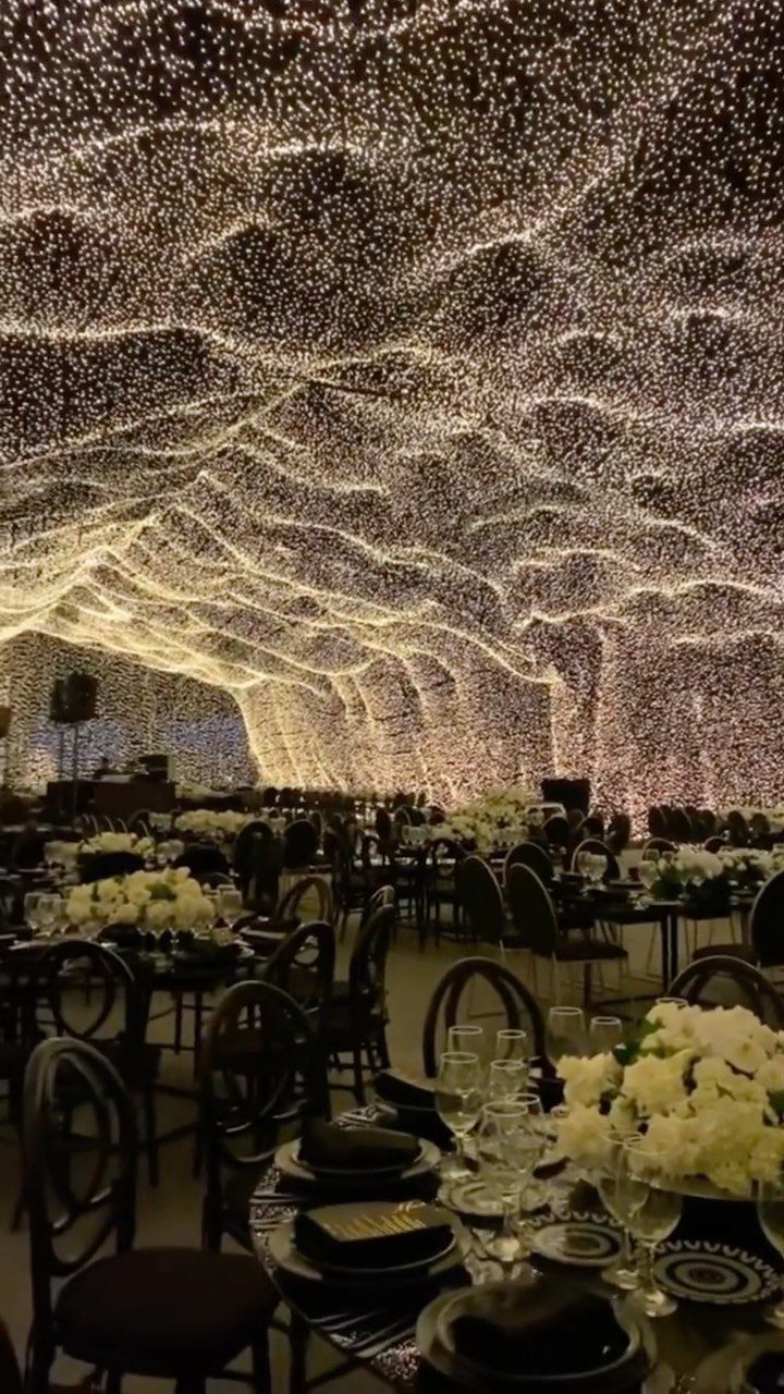 A banquet hall with a ceiling made of flowing, wavy layers of warm fairy lights.