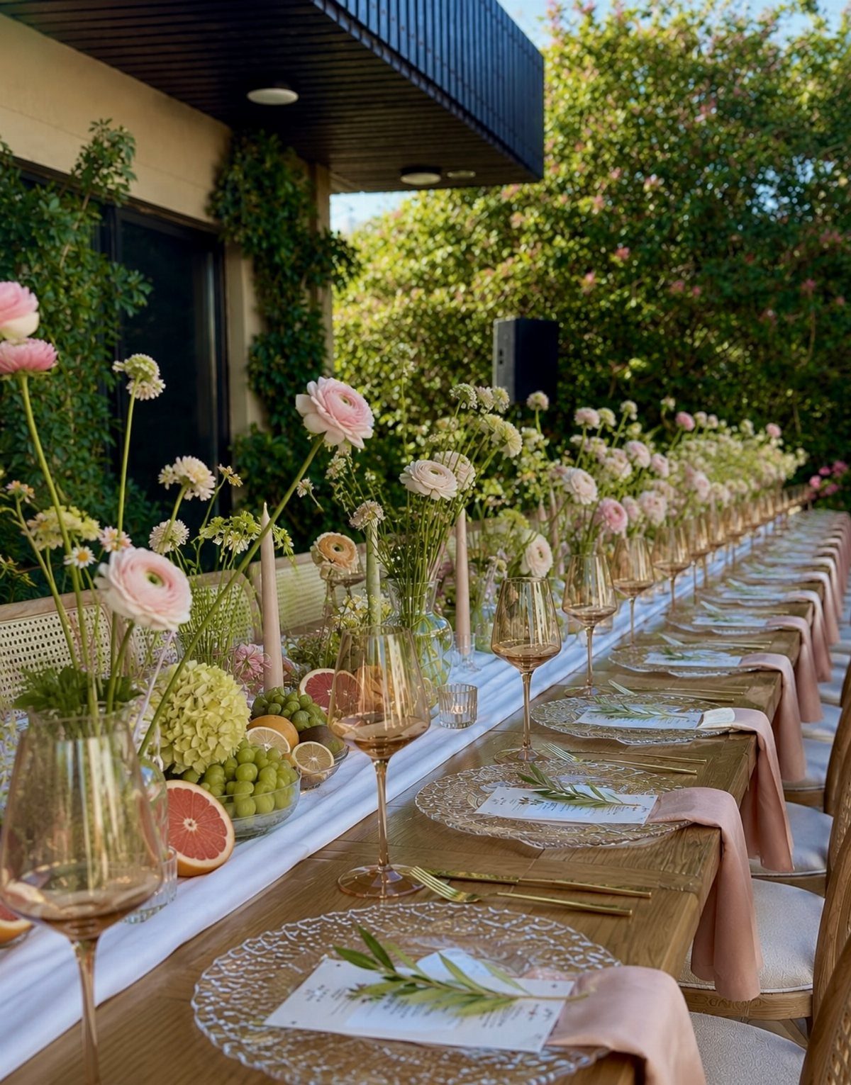 A long outdoor wedding table set with pink flowers, elegant glassware, and white linens.