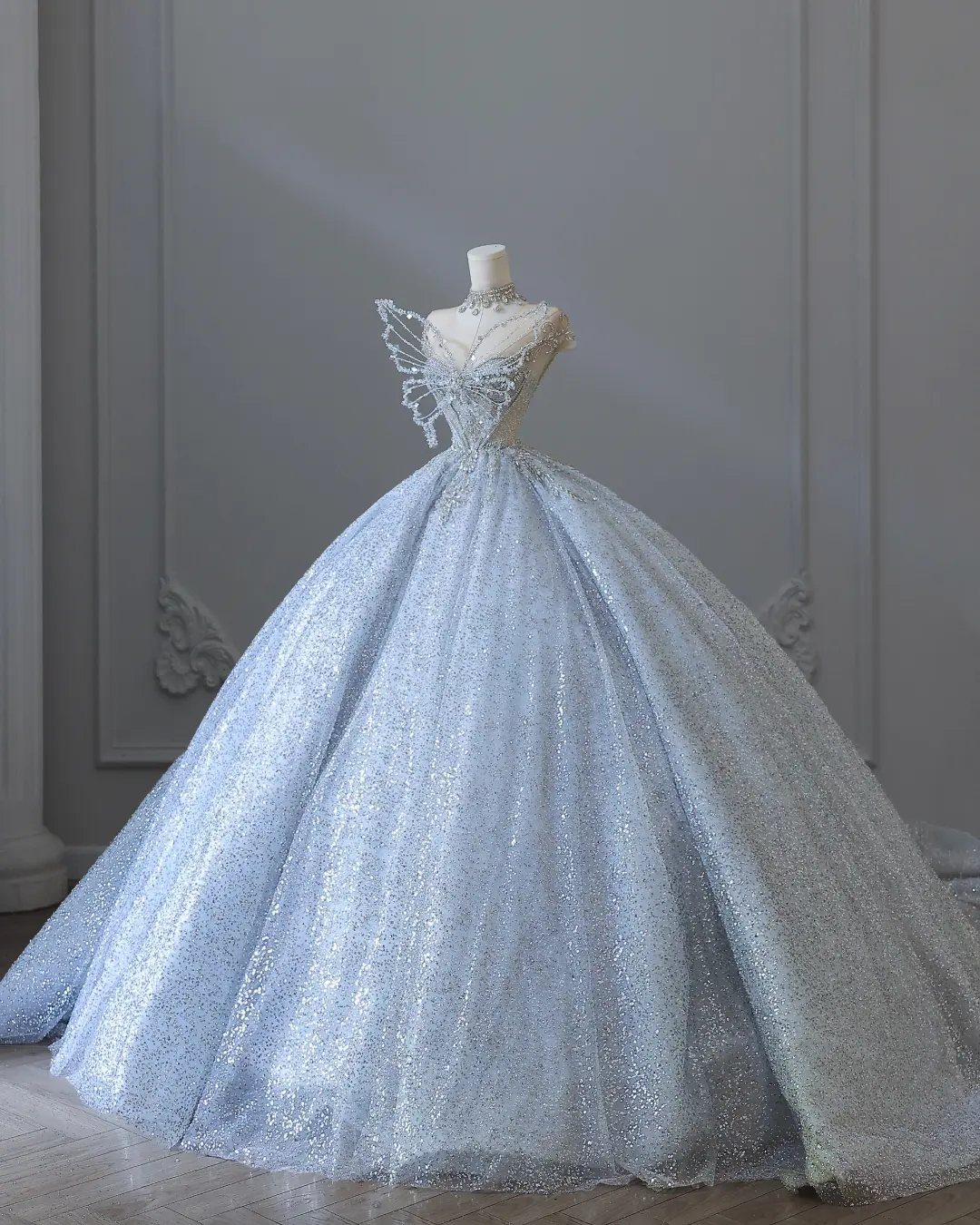 A shimmering light blue ball gown wedding dress with wing-like bodice details on a mannequin.