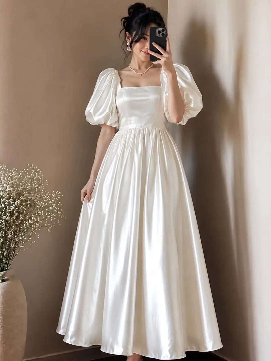Woman in an ivory satin wedding dress with puffy sleeves taking a mirror selfie.