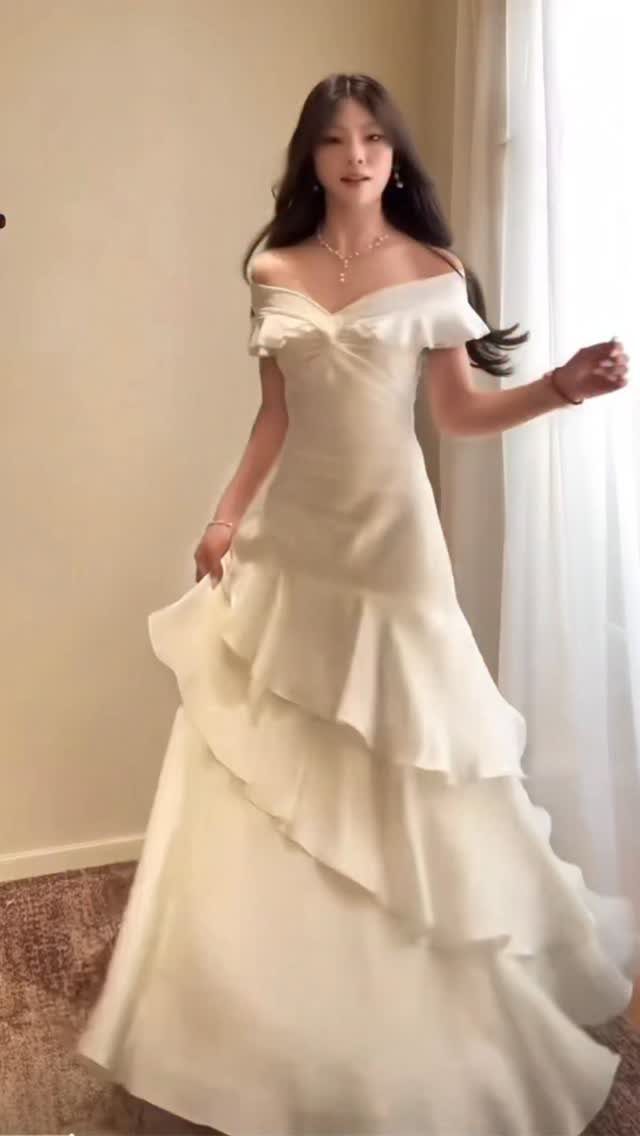 A woman posing in an ivory off-the-shoulder wedding dress with a tiered skirt.