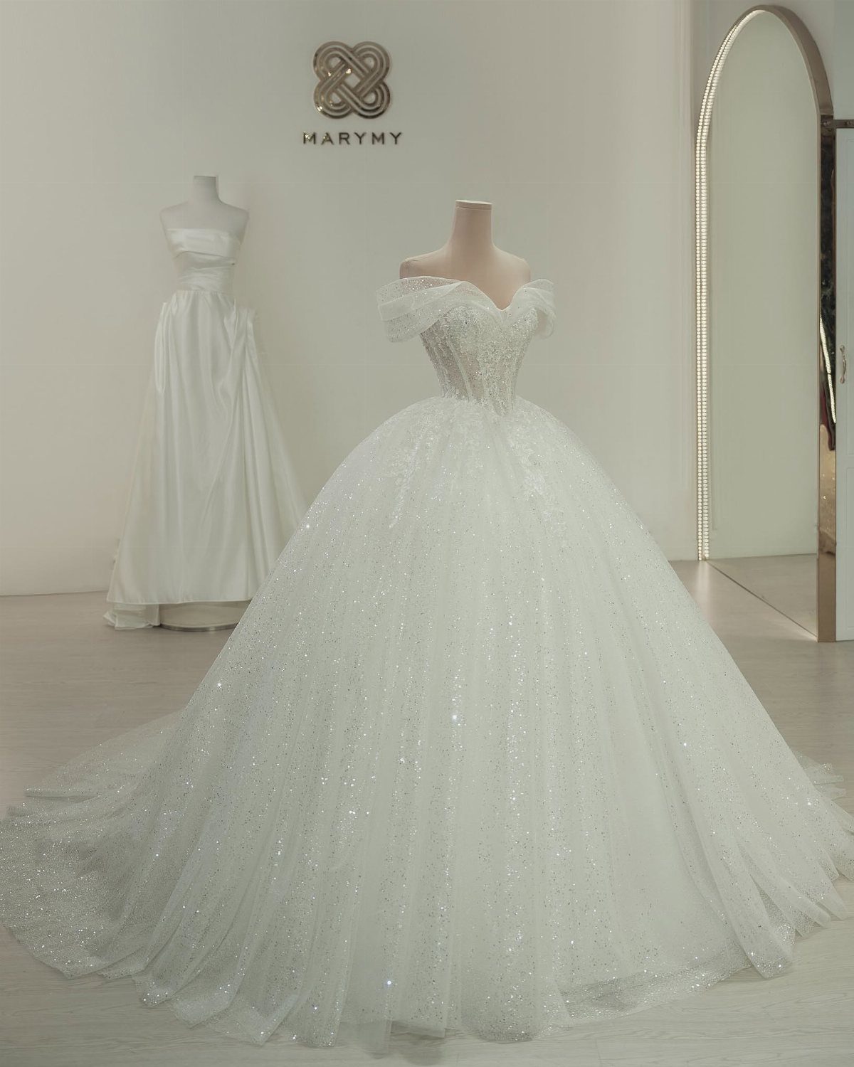 A sparkling white off-the-shoulder ball gown wedding dress displayed on a mannequin.