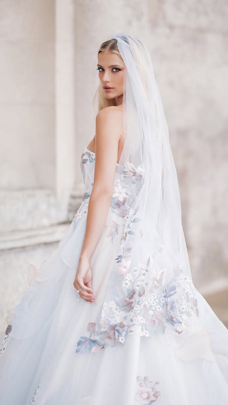 A woman wearing a white floral wedding gown and a long sheer veil.