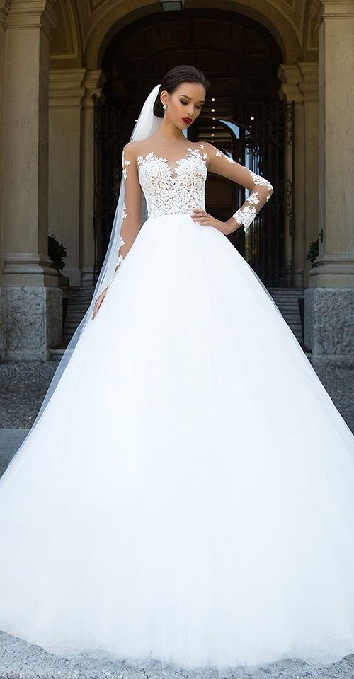 7 Wedding Dresses for Winter Brides That Balance Warmth and Style 2 Woman wearing a white lace wedding dress with long sleeves and a full tulle skirt.