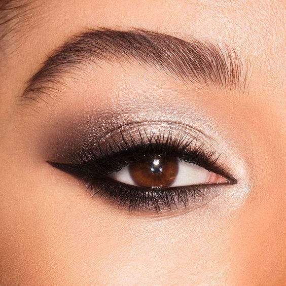 Close-up of a brown eye with dramatic dark charcoal and shimmering champagne eyeshadow.
