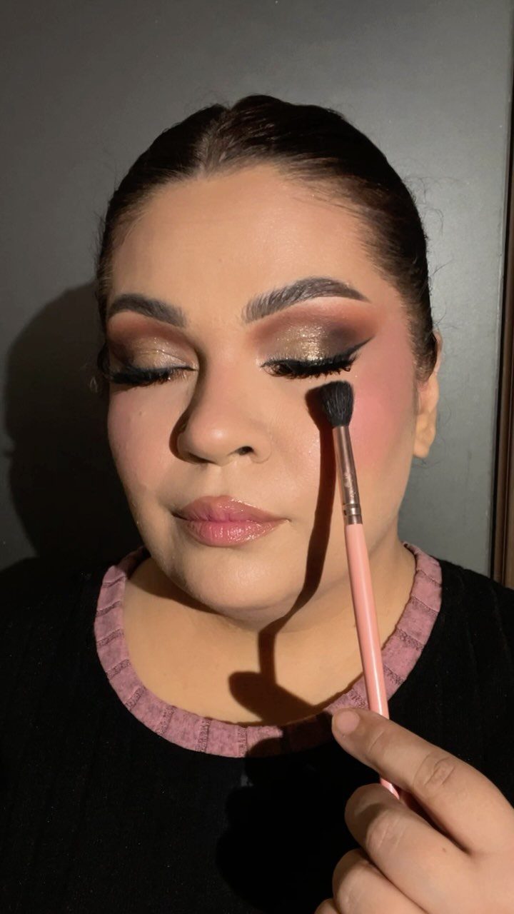 Woman with shimmering bronze and gold eyeshadow being applied with a pink makeup brush.