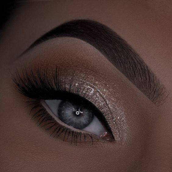 Close-up of a human eye with shimmering champagne eyeshadow and long dark eyelashes.