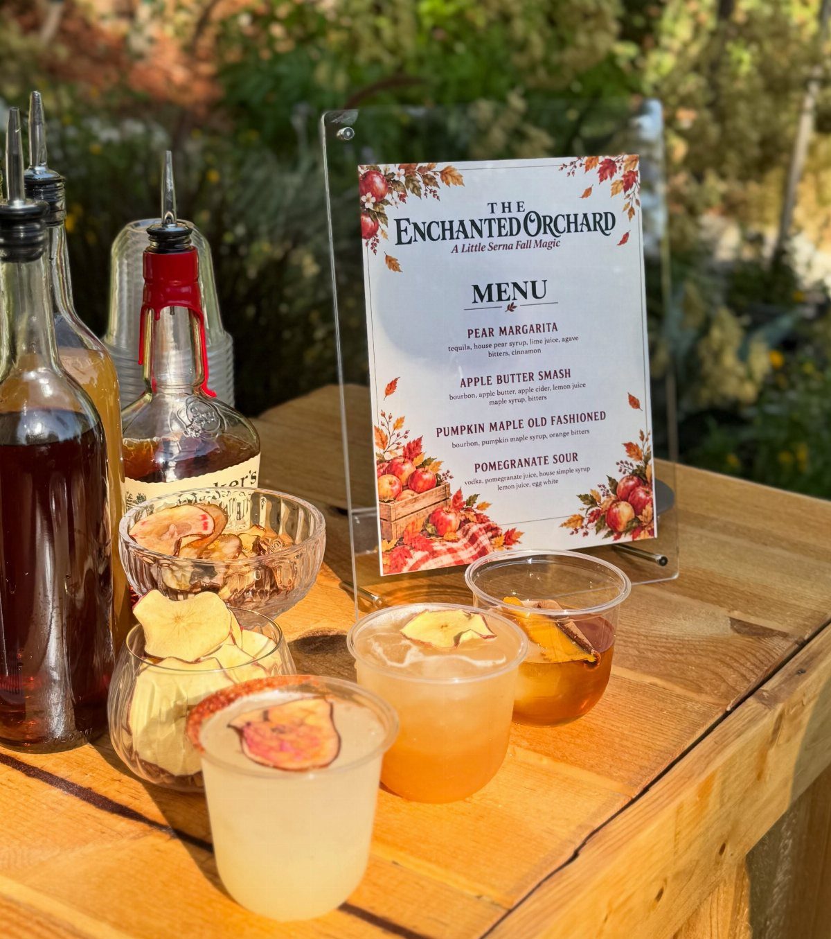 Three garnished apple cider cocktails sit on a wooden table next to a drink menu.