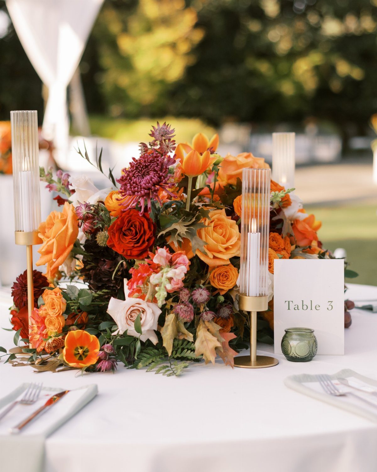 Autumnal floral centerpiece with orange and red flowers on a white wedding table.