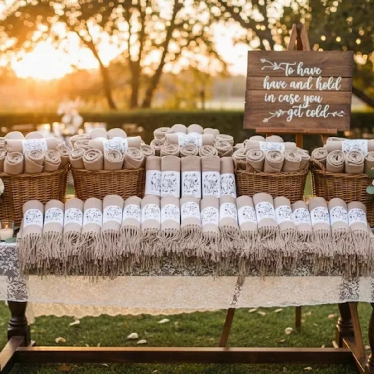 Rolled beige blankets with decorative bands arranged in baskets on a lace tablecloth outdoors.