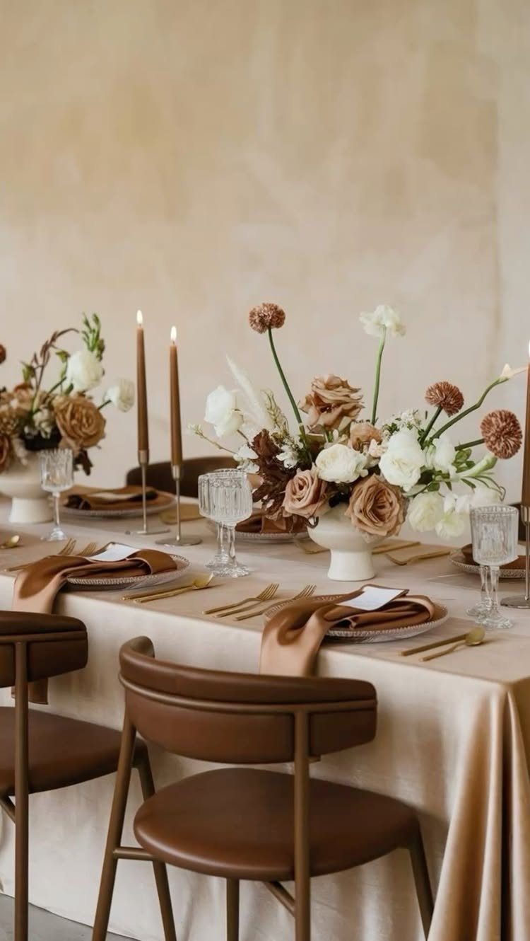 A formal dining table set with cream linens, tan napkins, and autumnal floral arrangements.