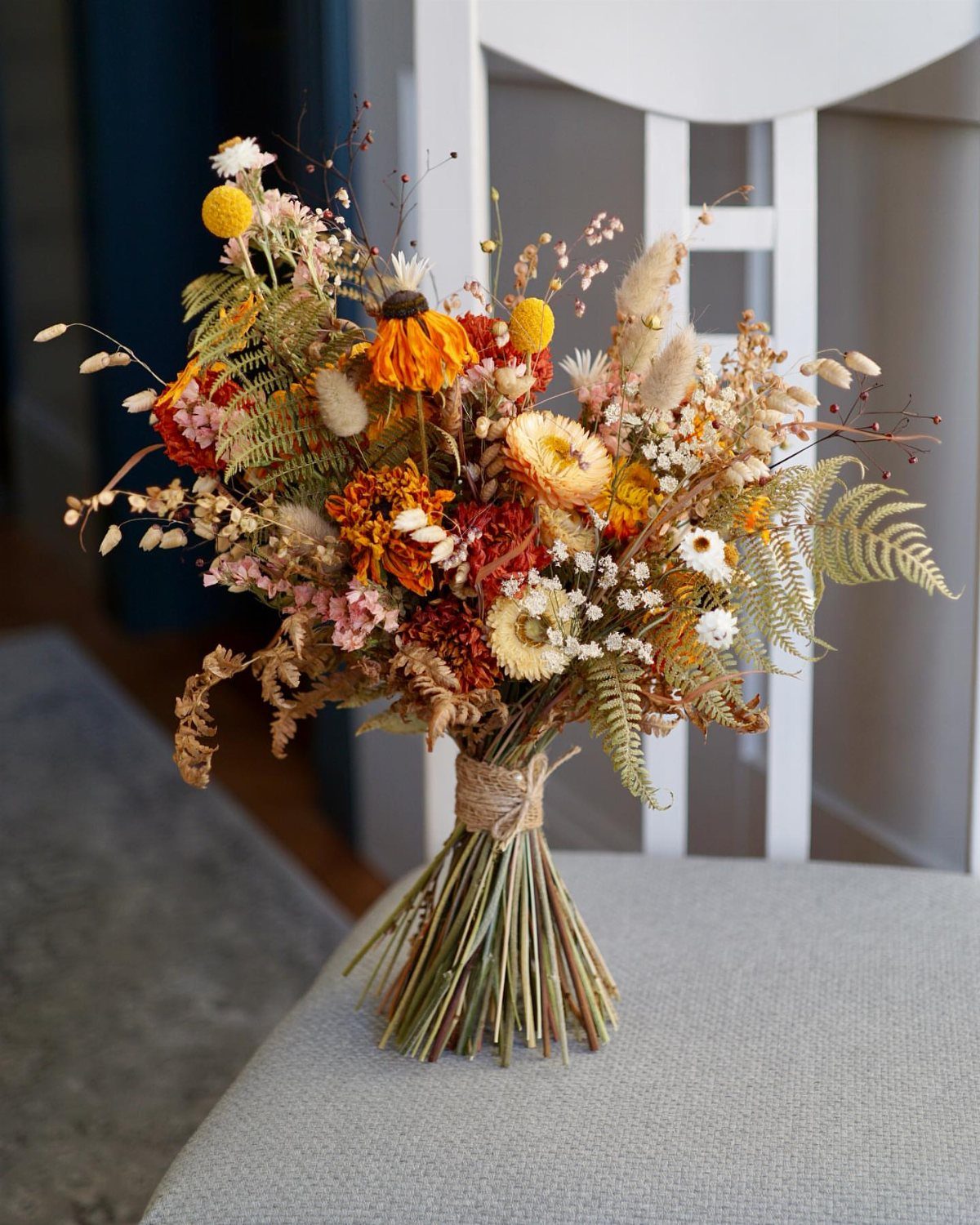 A dried floral bouquet with orange and yellow flowers tied with twine on a chair.