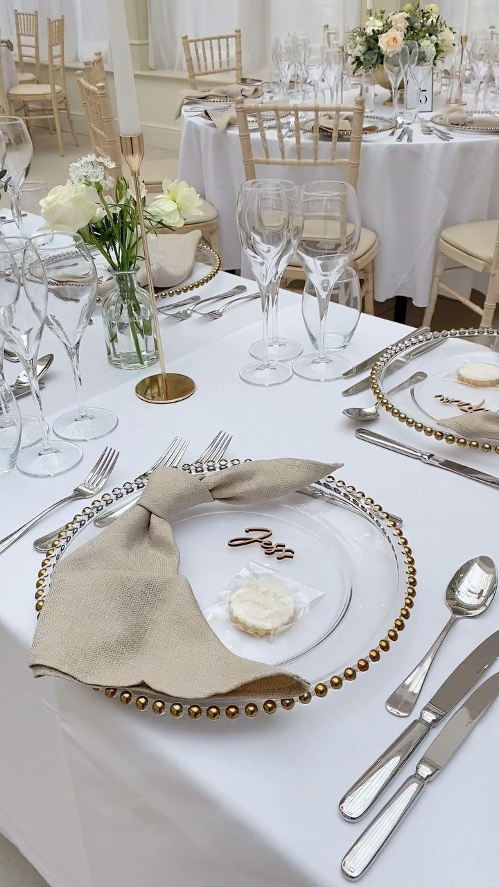 Formal wedding table setting with gold beaded glass plates, silverware, and white floral centerpieces.