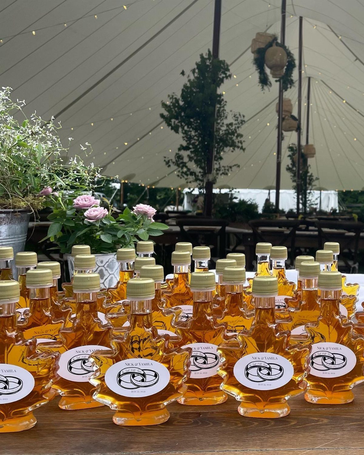 Small maple-shaped glass bottles filled with amber syrup arranged on a wooden table outdoors.