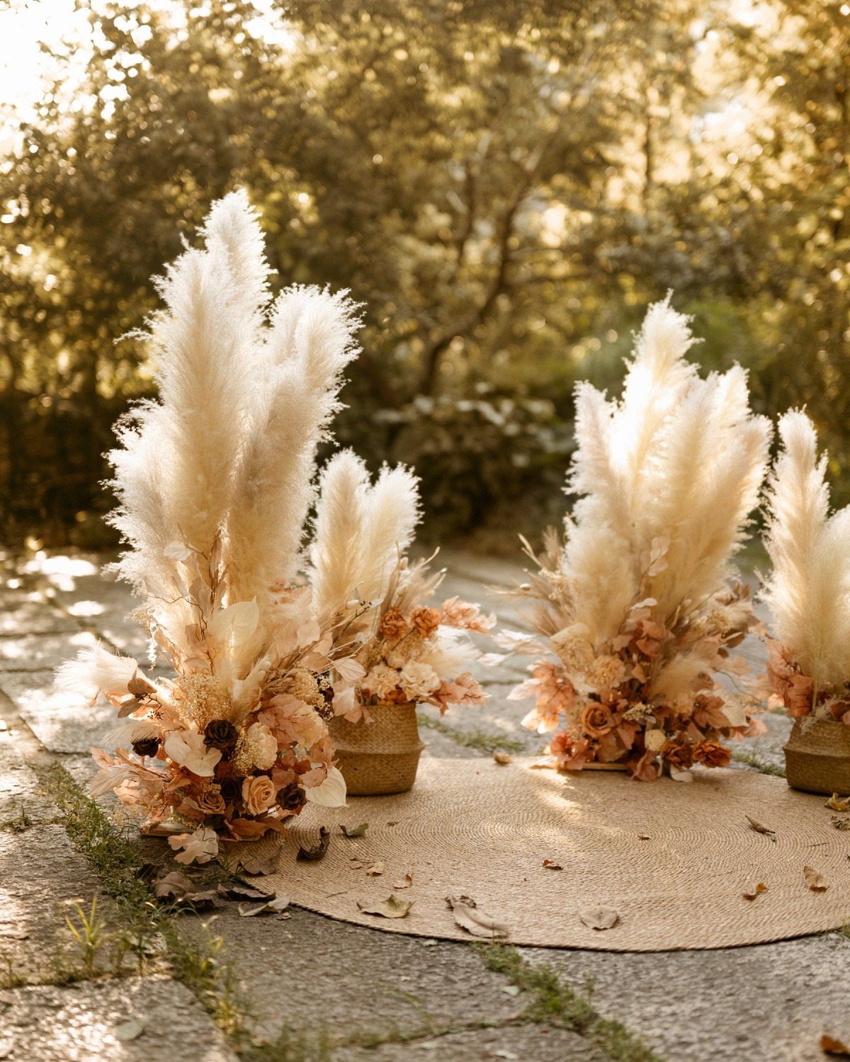 Large pampas grass arrangements with peach flowers arranged on a burlap runner outdoors.