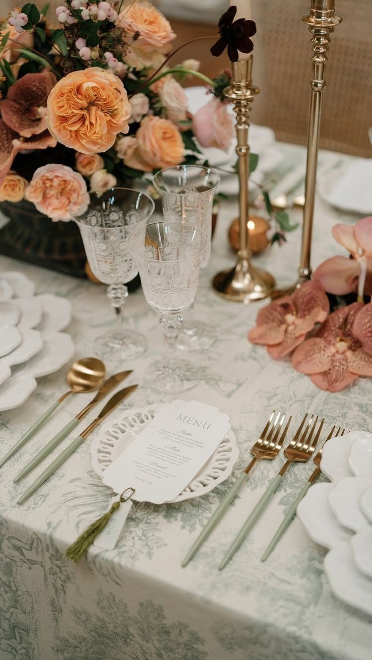Peach roses and crystal glassware arranged on a formal wedding table with gold cutlery.