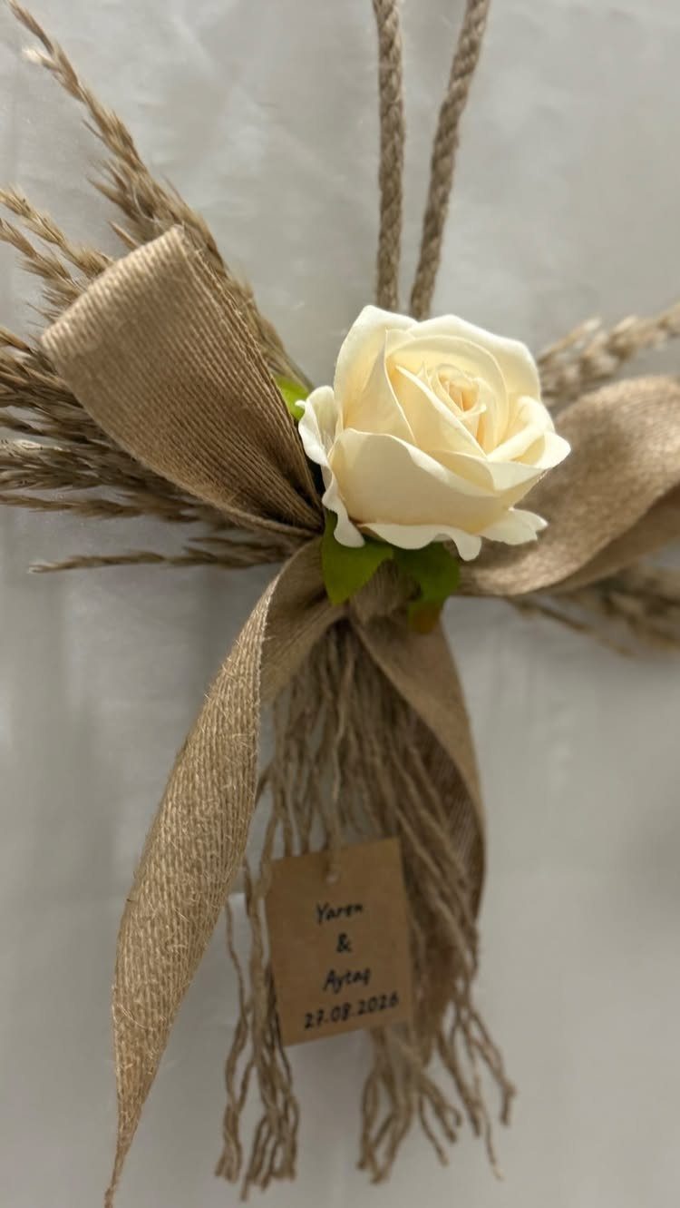 A white rose and burlap bow tied to dried wheat stalks with a name tag.