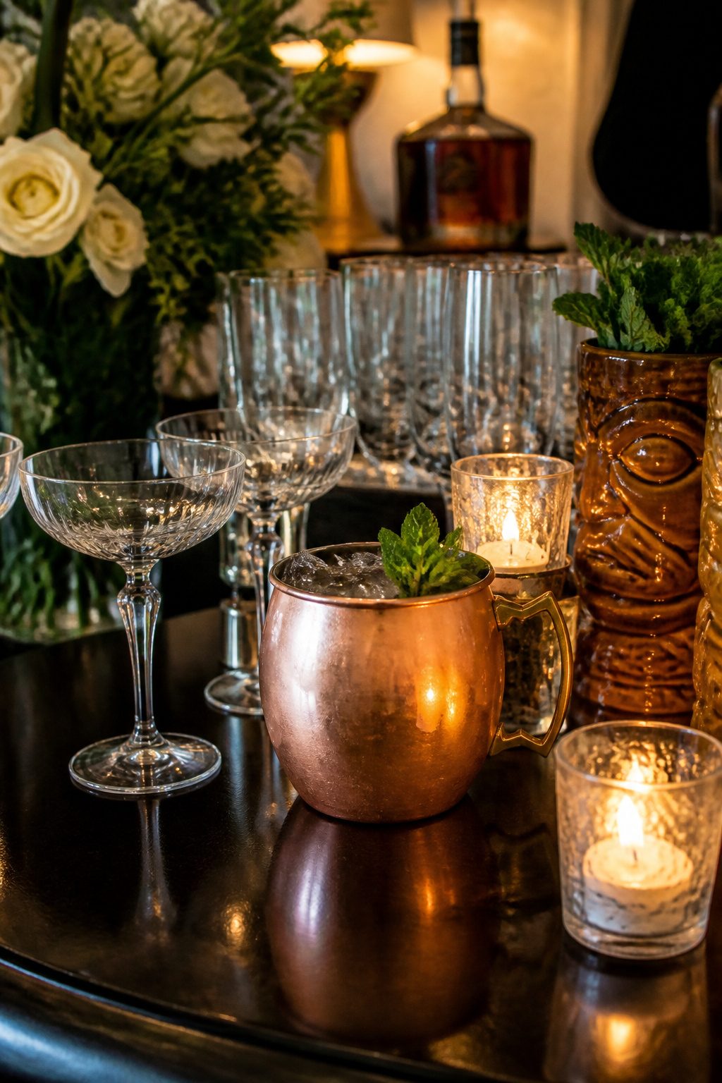 A copper Moscow Mule mug surrounded by cocktail coupes and champagne flutes.