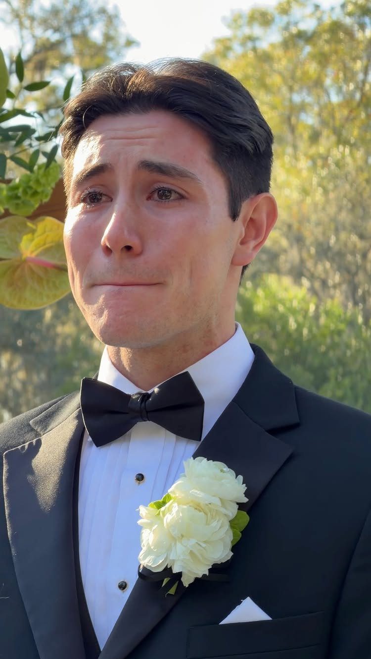 12 Wedding Groom Photos to Capture: From Getting Ready to Golden Hour 2 A groom in a black tuxedo looking emotional with tears in his eyes outdoors.