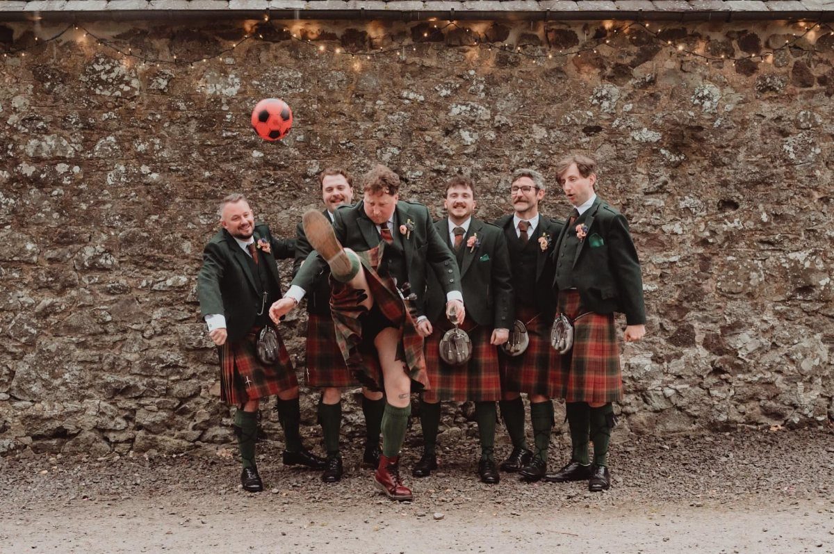 12 Wedding Groom Photos to Capture: From Getting Ready to Golden Hour 3 Six men in traditional Scottish kilts playing with a soccer ball against a stone wall.