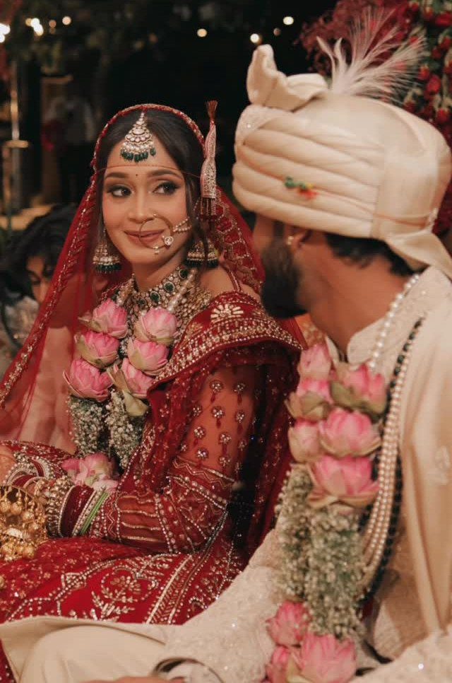 12 Wedding Groom Photos to Capture: From Getting Ready to Golden Hour 6 An Indian bride in red traditional attire gazes lovingly at her groom during their wedding ceremony.
