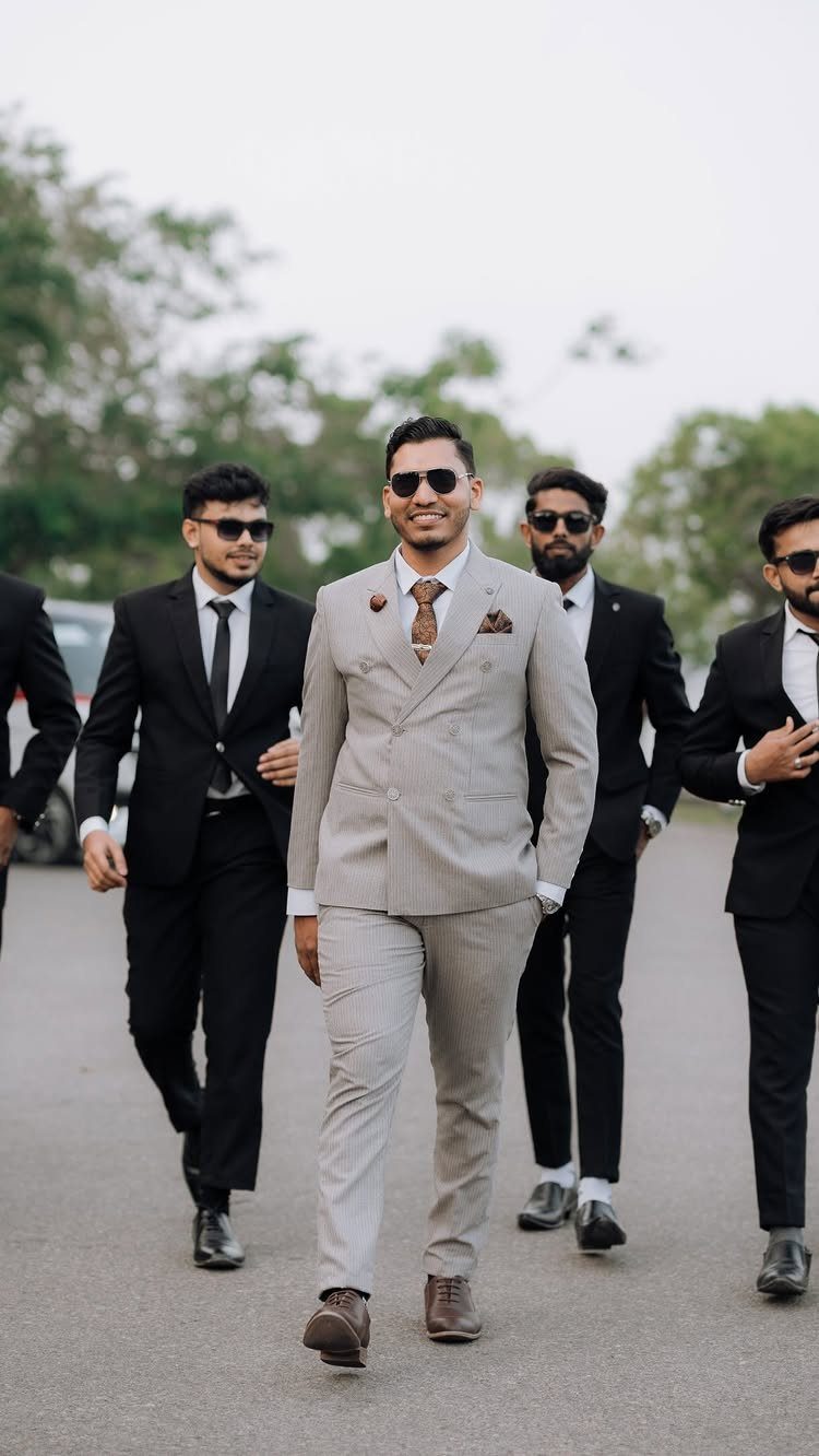 12 Wedding Groom Photos to Capture: From Getting Ready to Golden Hour 1 A groom in a grey suit walks forward accompanied by his groomsmen in black suits.