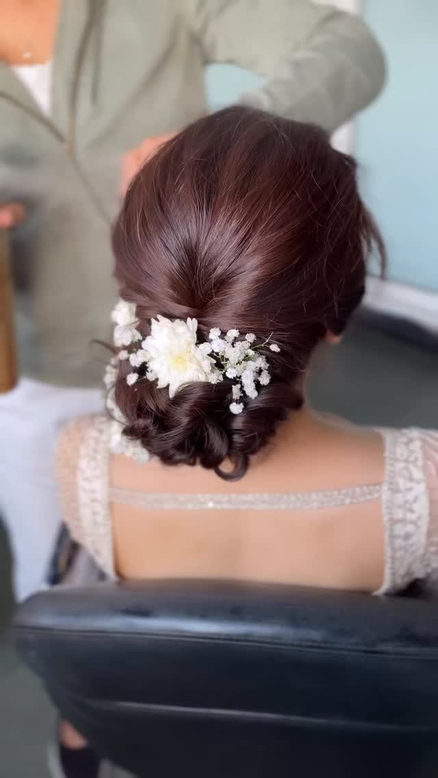 5 Wedding Hair Inspo Ideas for Brides From Loose Curls to Hollywood Waves 3 A woman's dark hair styled in a low twisted bun decorated with white flowers.