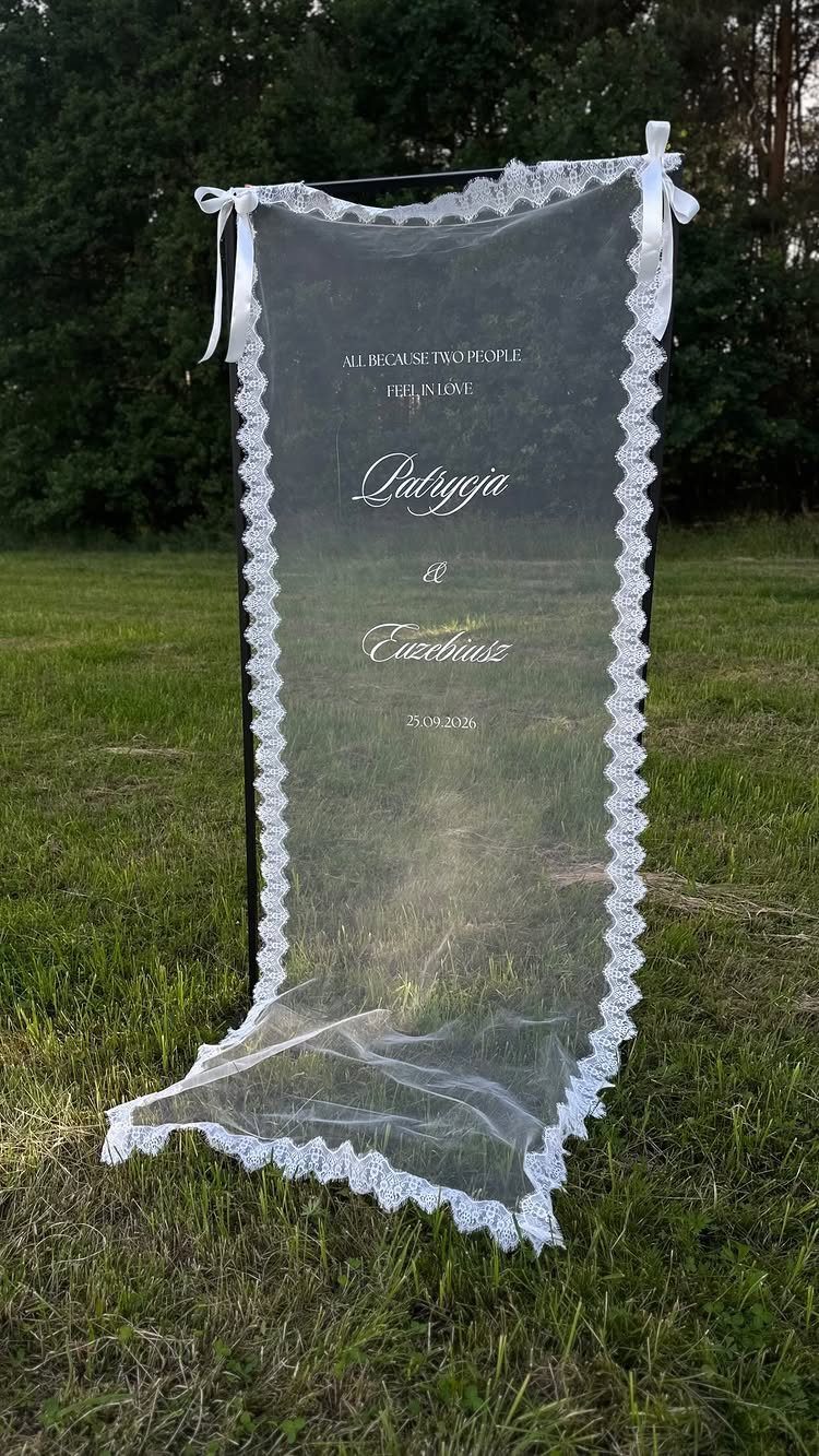 A white lace-trimmed veil with printed text hanging on a bar in a grassy field.