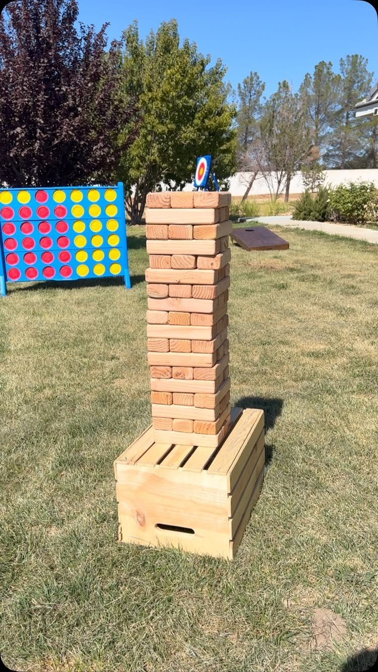 Wooden block tower on a crate with lawn games in a grassy backyard setting.