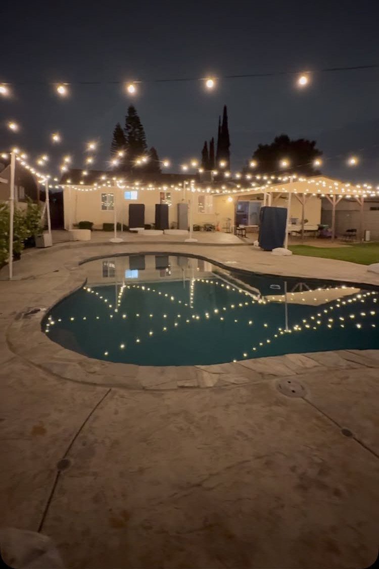 String lights hanging over a backyard swimming pool and patio area at night.