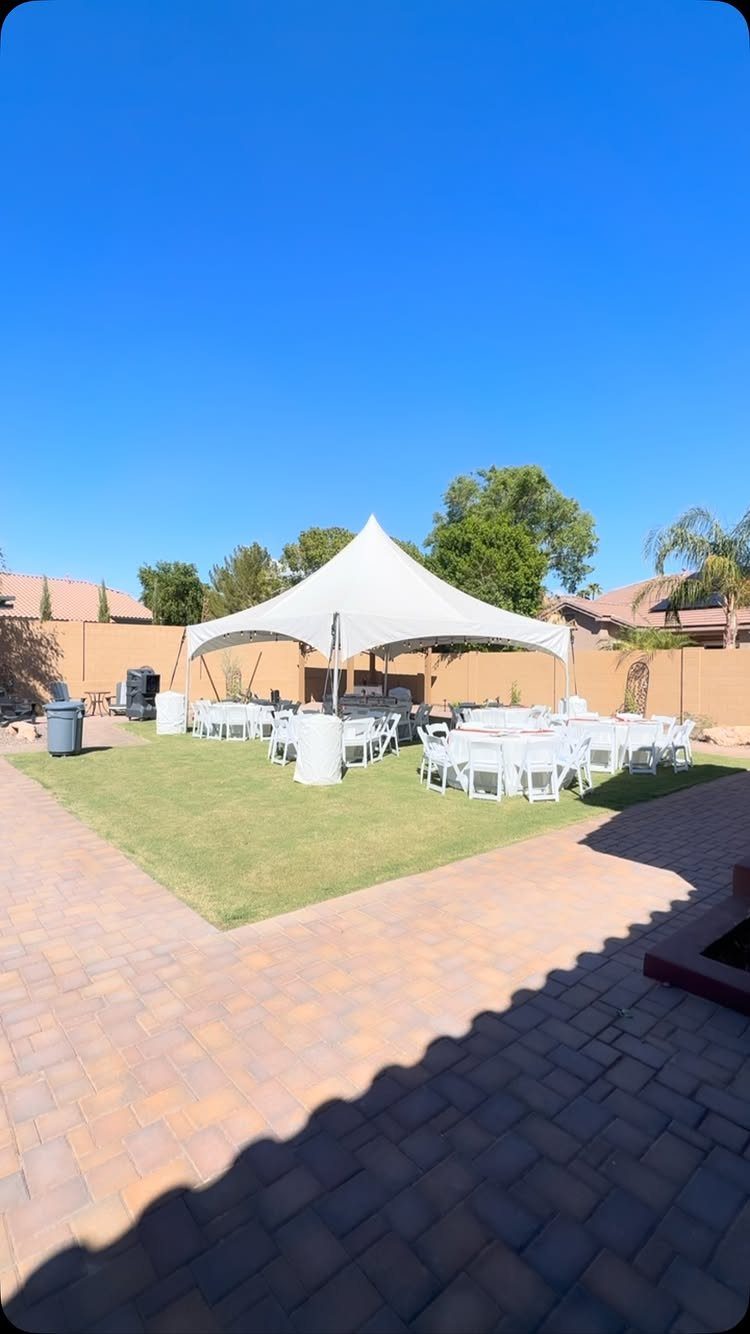 A white event tent set up on a lawn with several round tables and white chairs.