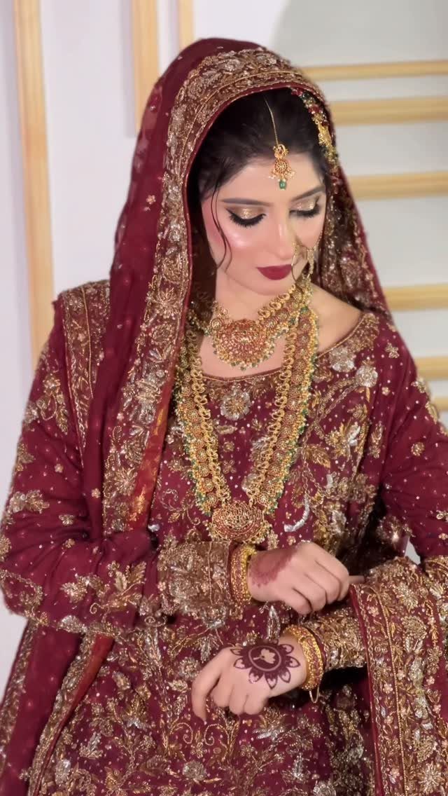 A bride wearing maroon traditional clothing and heavy gold jewelry with bold red lipstick.