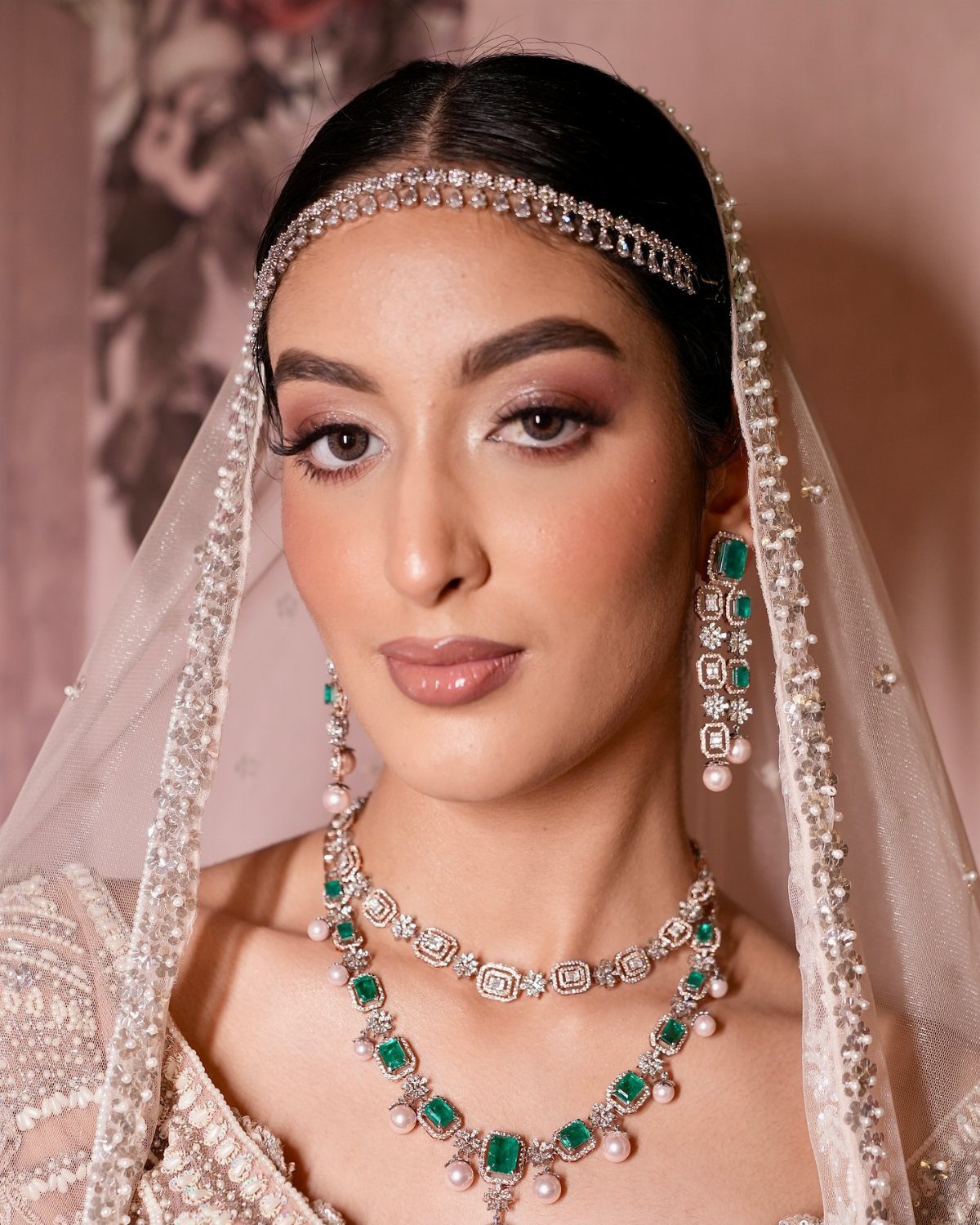 A bride with shimmering eye makeup, wearing emerald jewelry and a beaded veil.