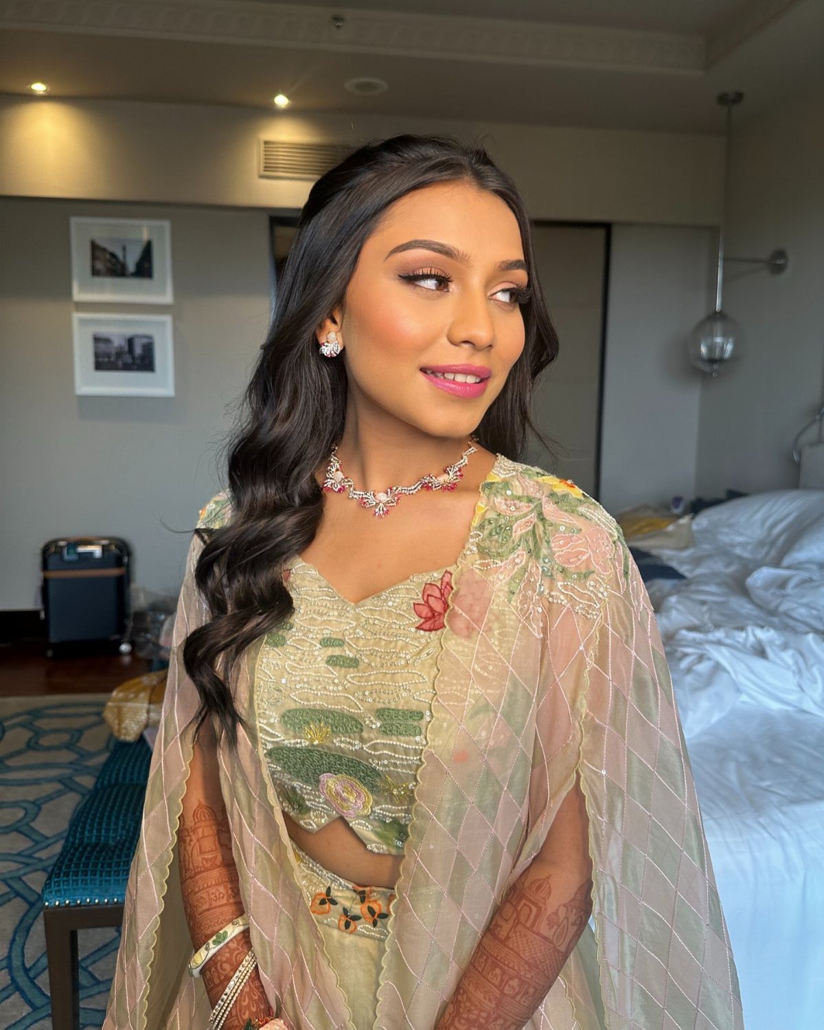 A young woman with glowing makeup and wavy dark hair wearing traditional green attire.