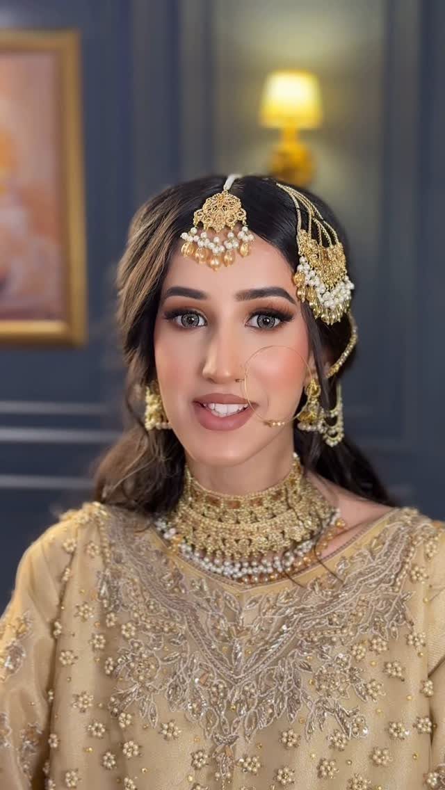 A bride with heavy gold jewelry and glamorous wedding makeup looking towards the camera.