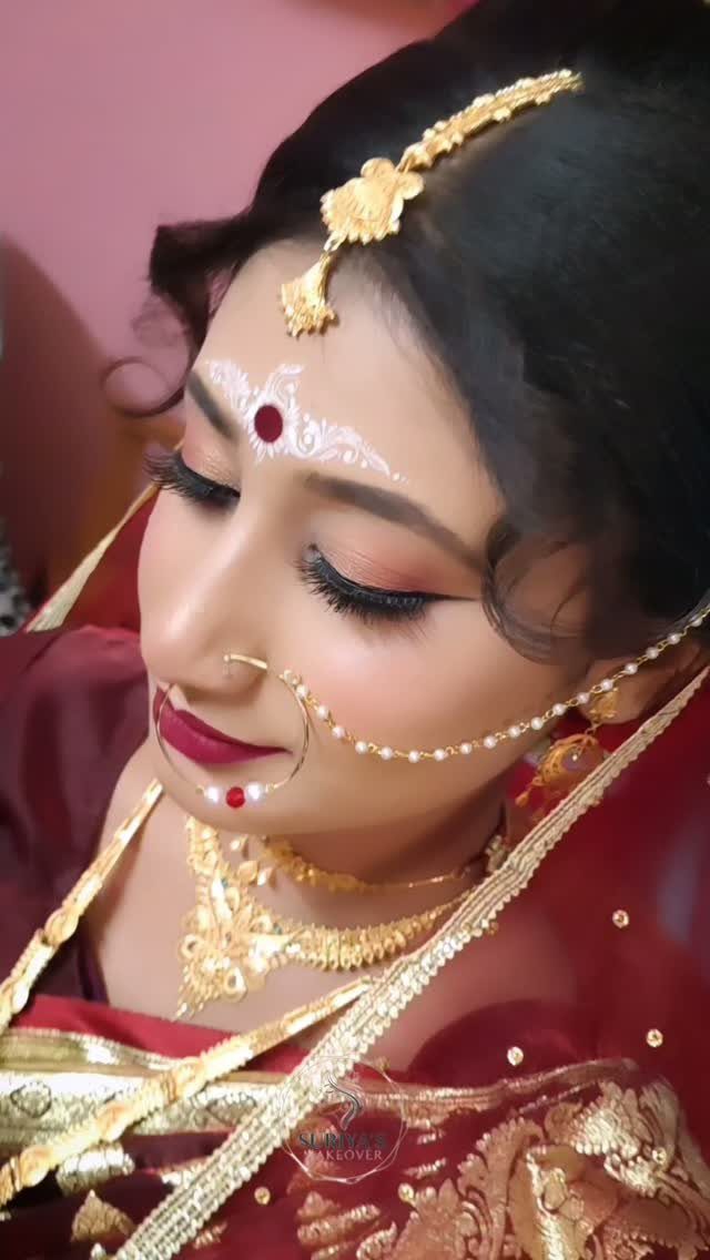 A bride with traditional Indian wedding makeup and gold jewelry looking downwards.