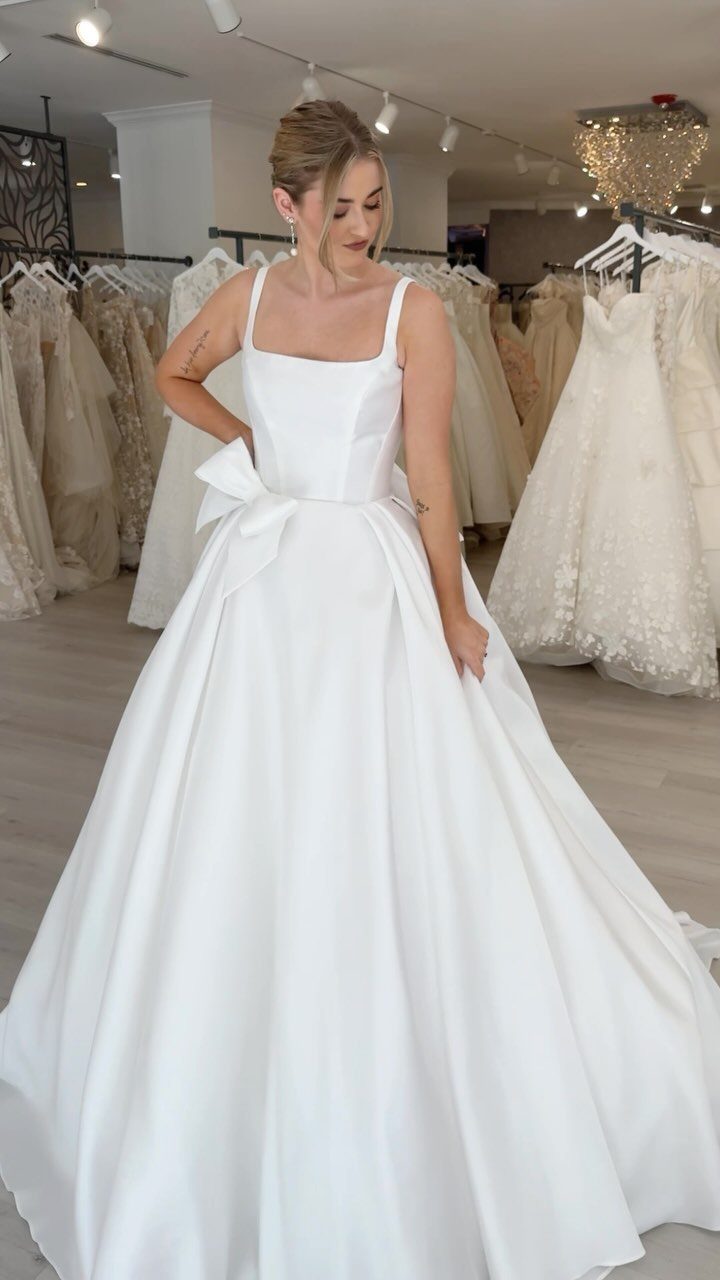 Wedding Outfit for Europe: 6 Ideas for 2026 Ceremonies Abroad 4 A woman wearing a white satin A-line wedding dress with a large bow at the waist.