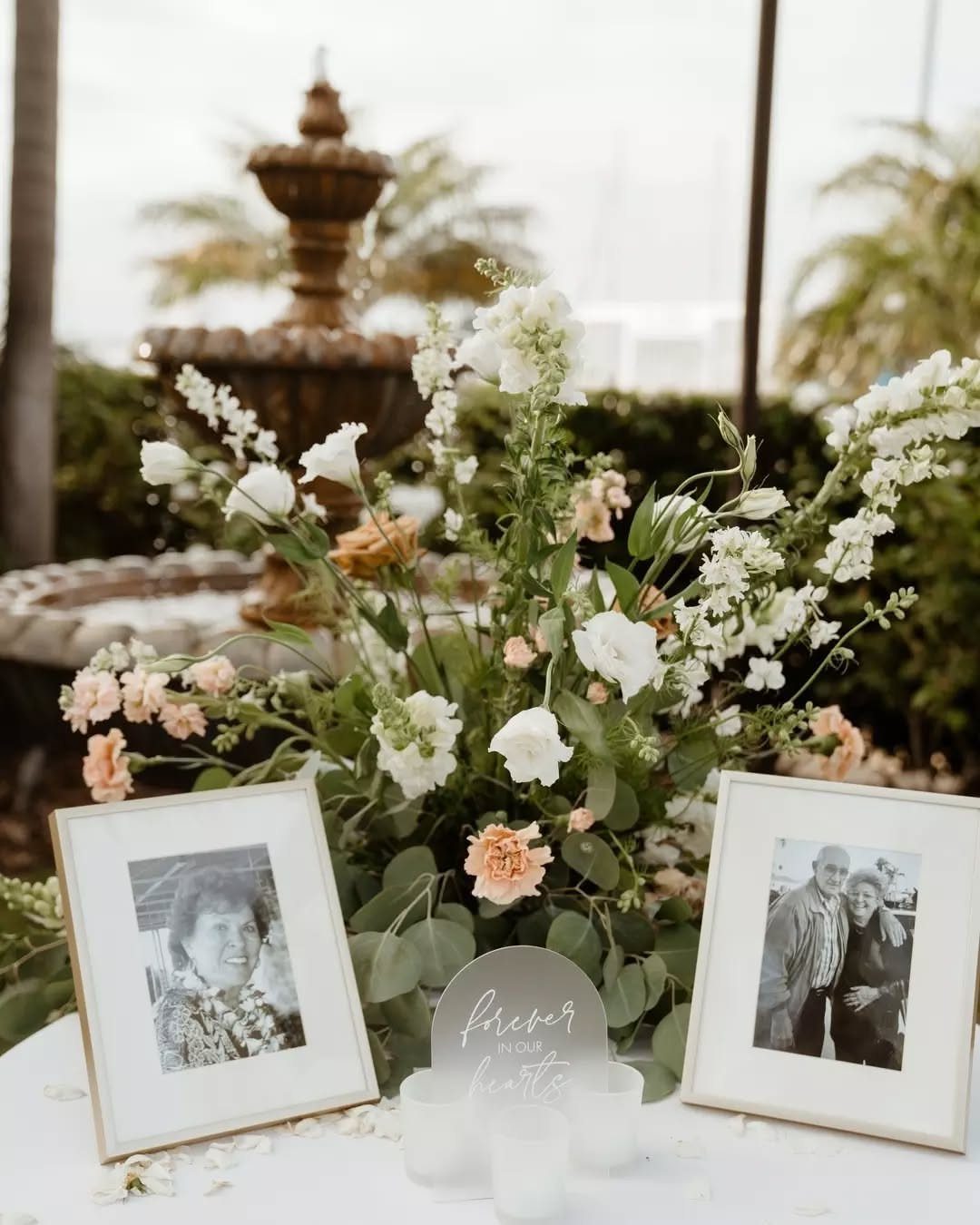 White and peach floral arrangement on a table with framed photographs and small white candles.