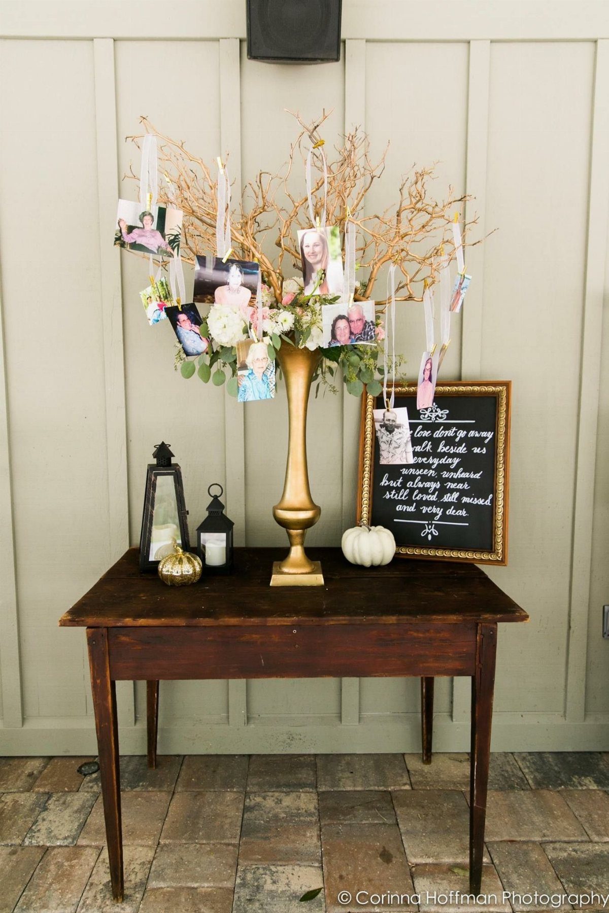 Branches with hanging photographs in a gold vase on a wooden table.
