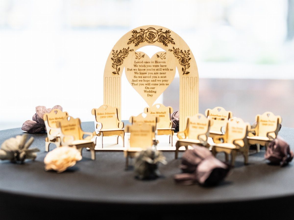 Laser-cut wooden memorial sign with miniature chairs on a dark tabletop.