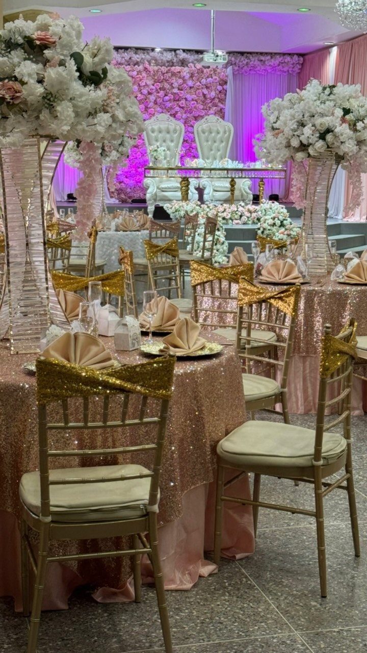 Wedding reception tables with blush pink sequined cloths, gold chairs, and large white floral arrangements.