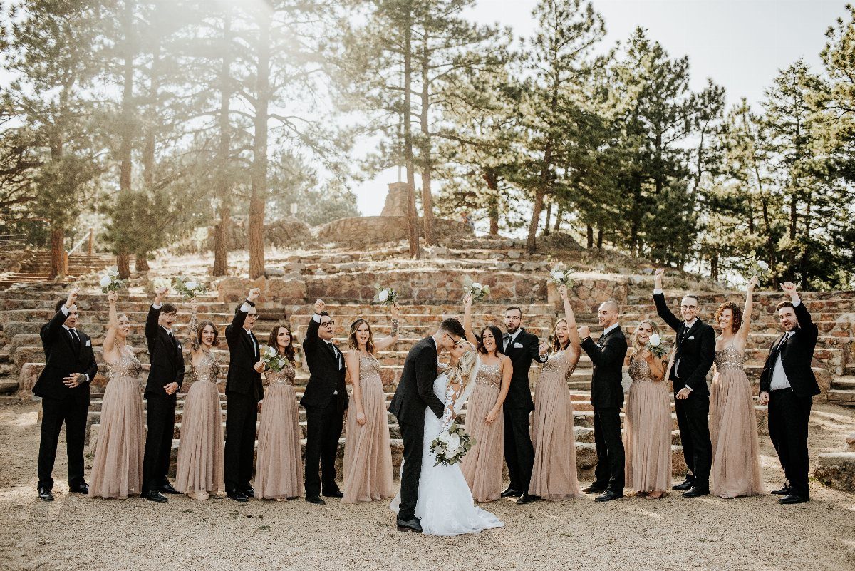 Wedding party posing outdoors with bridesmaids in champagne dresses and groomsmen in black suits.