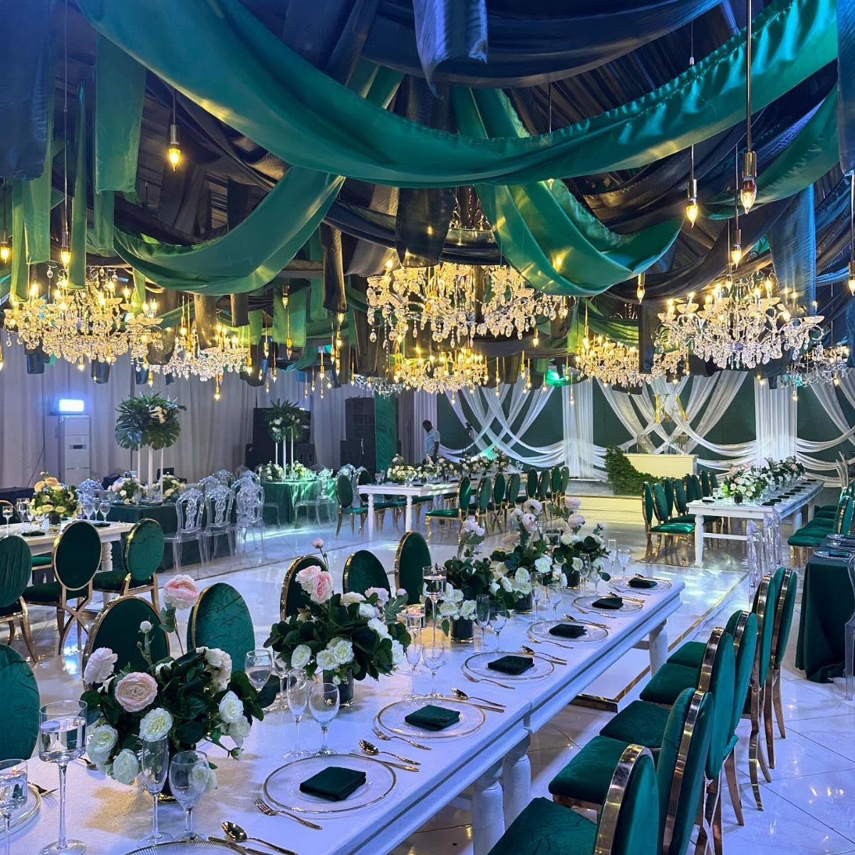 Emerald green fabric drapes and crystal chandeliers hang over white wedding tables with green accents.